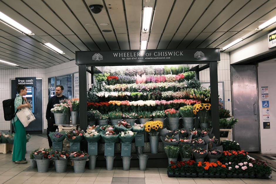 A vibrant display of fresh flower bouquets arranged on a black stand at Wheeler of Chiswick, located within a well-lit underground station. The arrangement includes a variety of colorful flowers such 